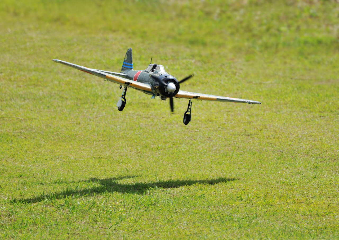 Image of a remote-controlled airplane flying along a field.