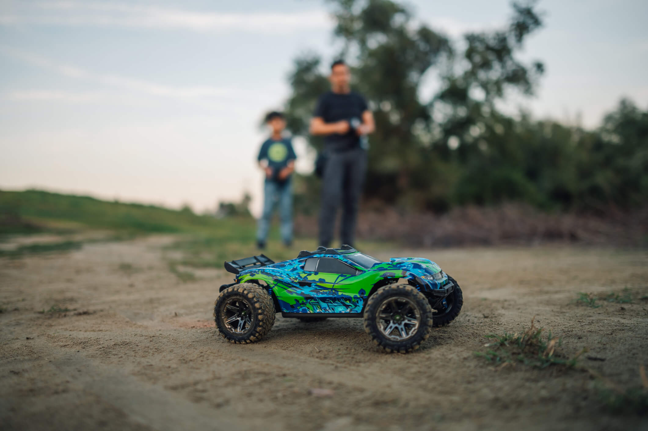 A close-up of a Traxxas Rustler 4x4 VXL on a dirt surface, featuring its rugged tires and vibrant blue and green body.